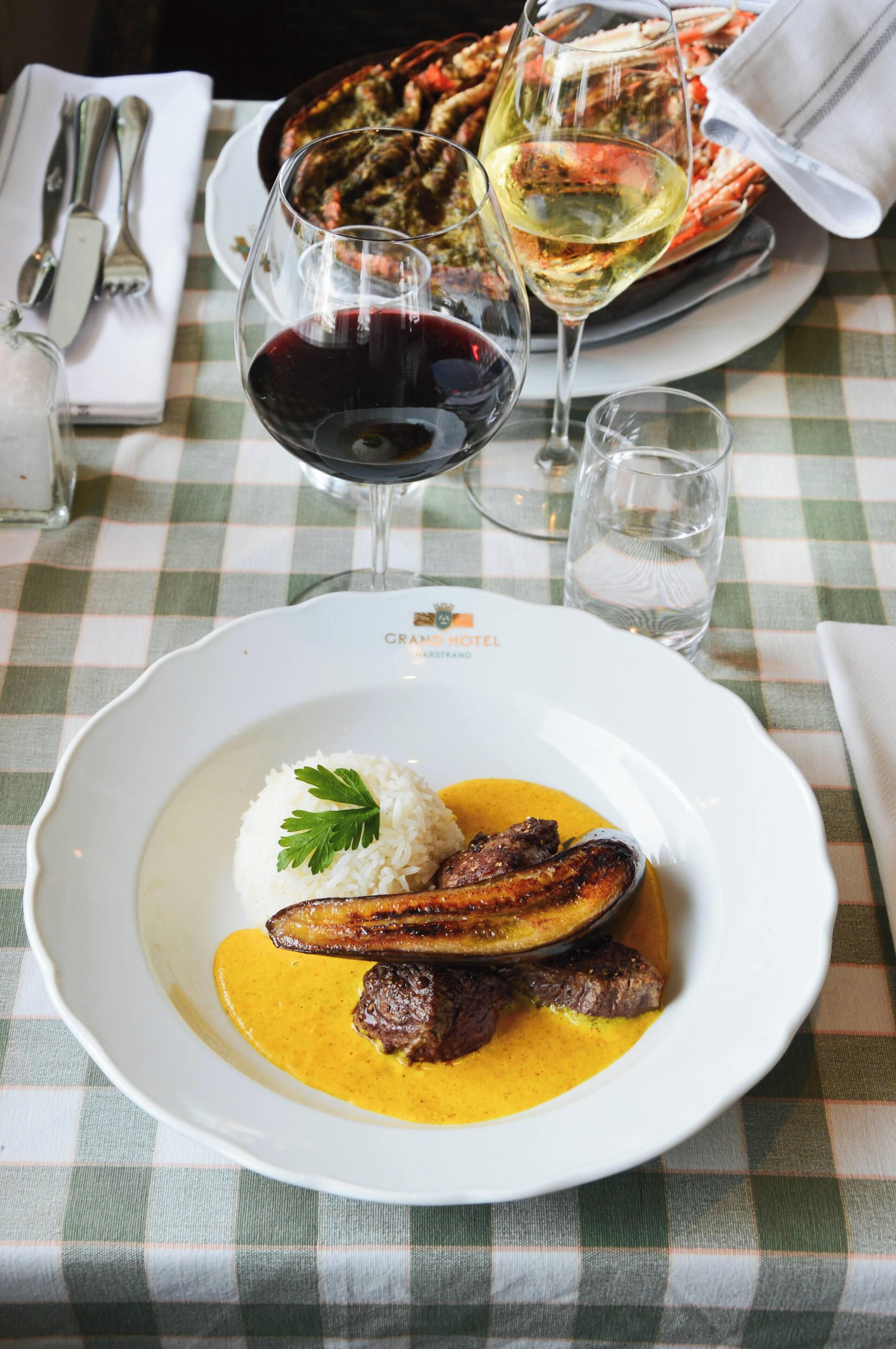 A table with a checkered tablecloth, a plate of food, and glasses of wine.