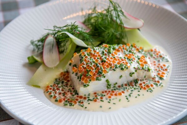 A white plate with a piece of fish topped with orange roe, green chives, and a creamy sauce. - Grand Hotel Marstrand (Marstrand)