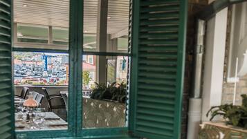 A dining area with a checkered tablecloth, a lamp, and a view through a window with green shutters.