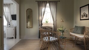 A room with a desk, wicker chairs, a sofa, a mirror, curtains, and a framed picture on the wall.