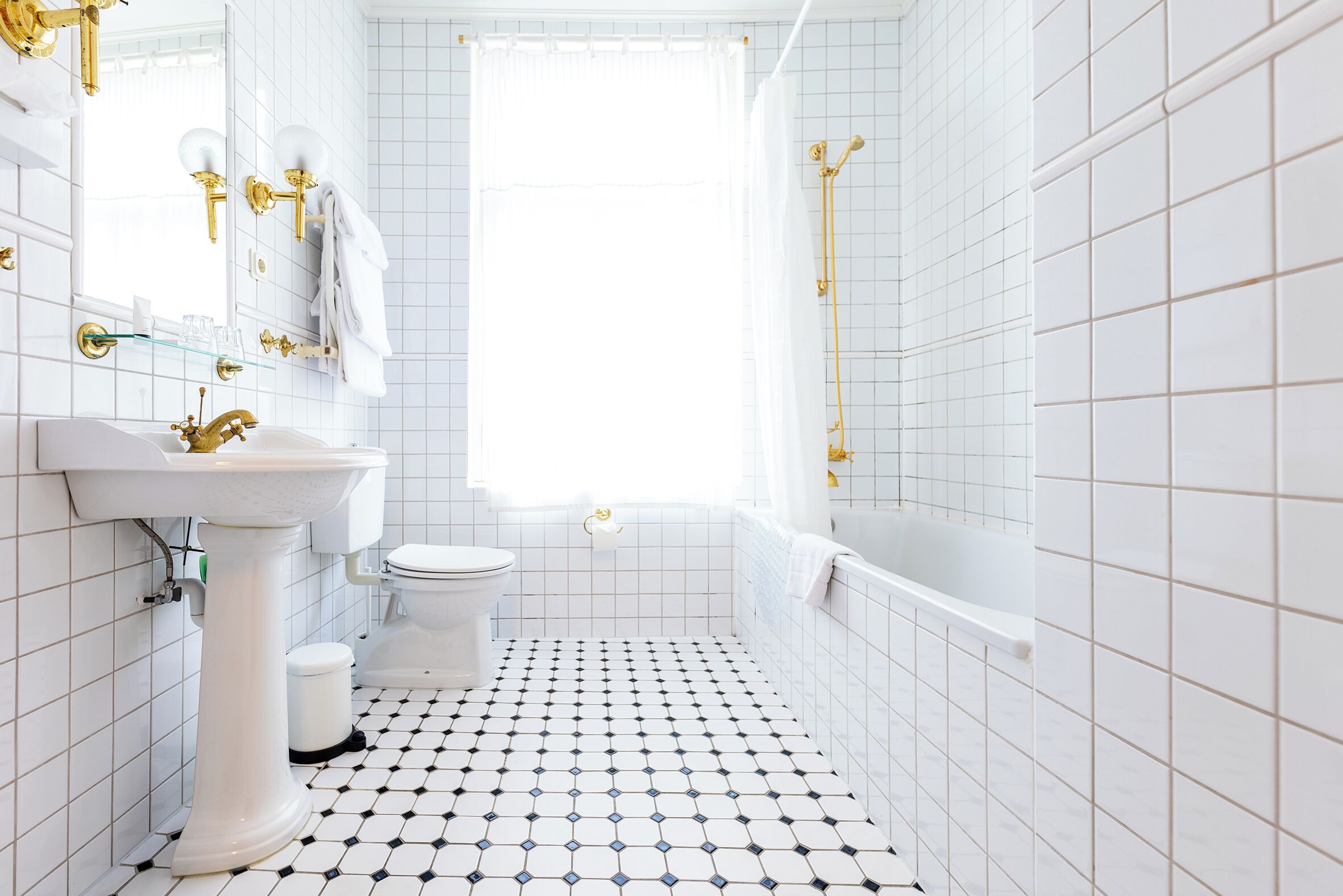 Un baño con lavamanos, inodoro y bañera blancos, suelo de baldosas y una ventana.