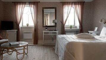 Quarto de hotel com cama, escrivaninha, cadeira, televisão e janela com cortinas.