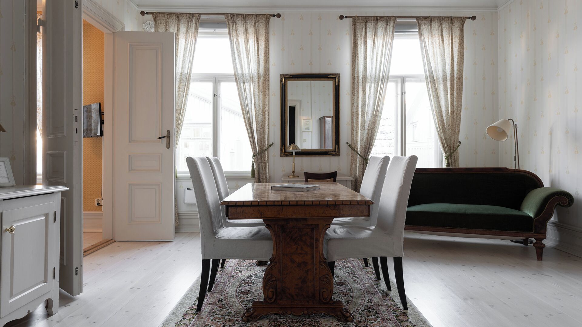 A dining room with a wooden table, white chairs, a green sofa, and a large mirror on the wall.