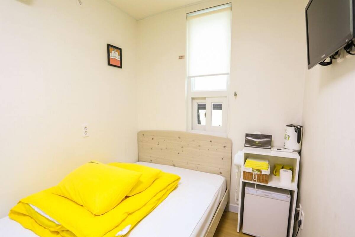 Ein kleiner, sauberer Raum mit Bett, Fenster, Fernseher und Küchenzeile.
