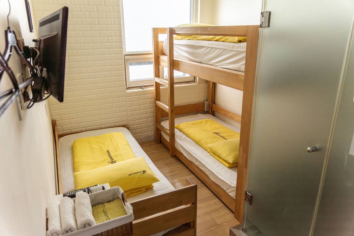 Ein Schlafraum mit Etagenbetten, Holzboden, Fenster, Wandfernseher und Schrank.