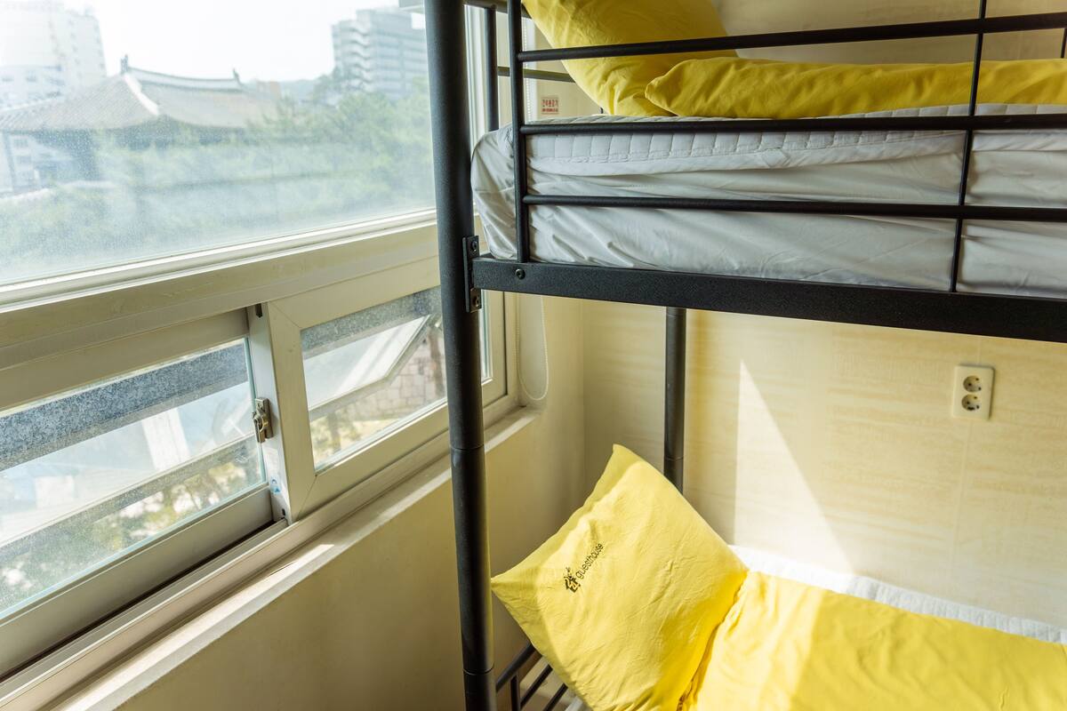 Ein Etagenbett mit gelben Kissen und einem Fenster mit Blick auf Gebäude.