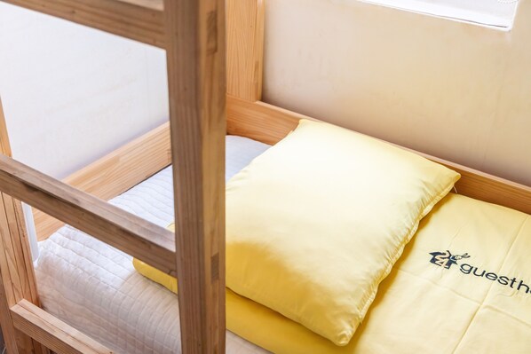 A wooden bunk bed with a yellow pillow and a bedspread with a logo.