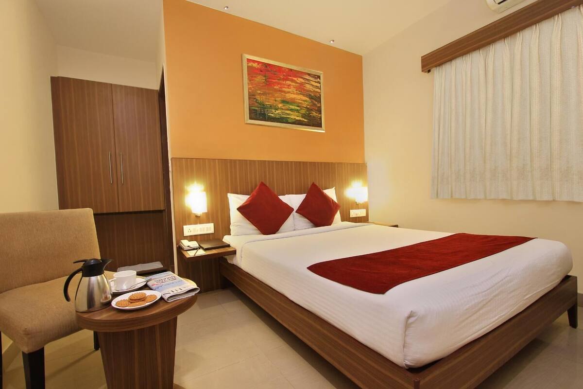 A hotel room with a bed, a nightstand, a chair, and a painting on the wall.