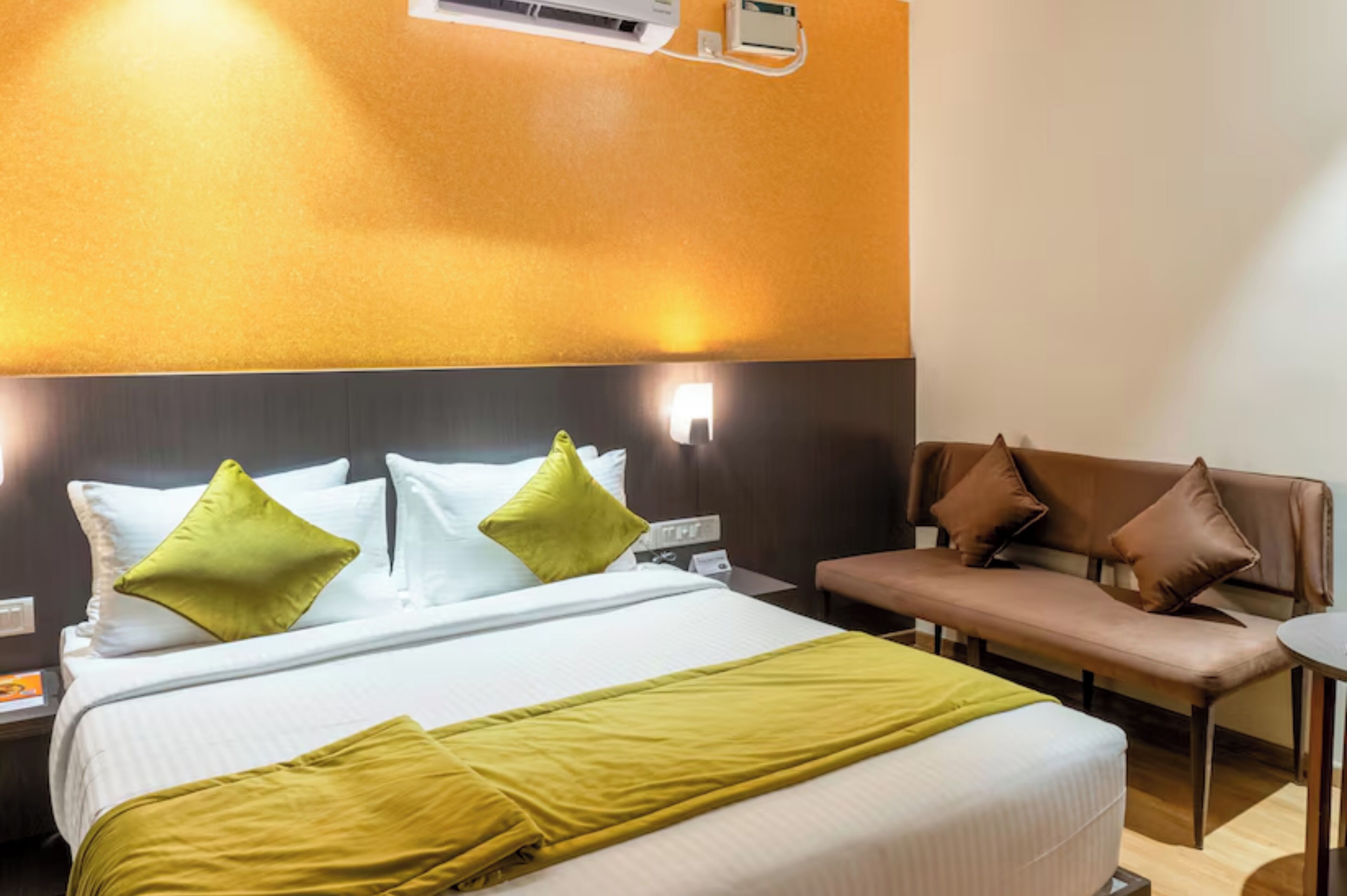 A hotel room with a bed, a bench, and a wall-mounted air conditioner.