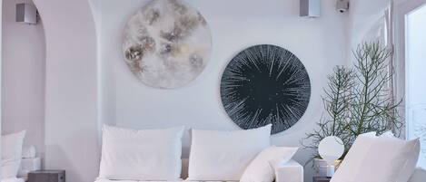 A modern living room with a white sofa, a coffee table with a fruit plate, and abstract wall art.