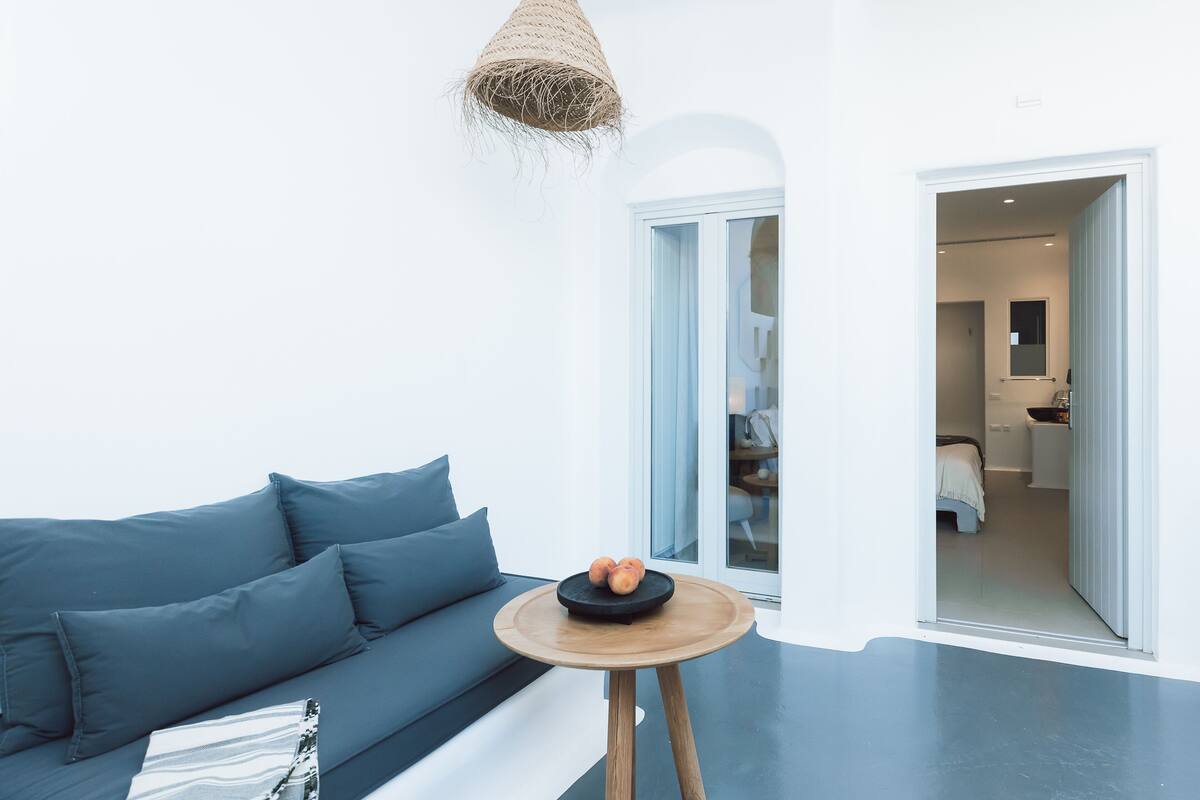 A modern living room with a blue sofa, a small wooden table with fruit, and a woven light fixture.