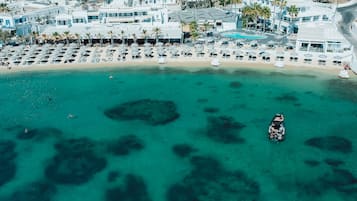 An aerial view of a coastal resort with a beach, clear turquoise waters, and a pool area.