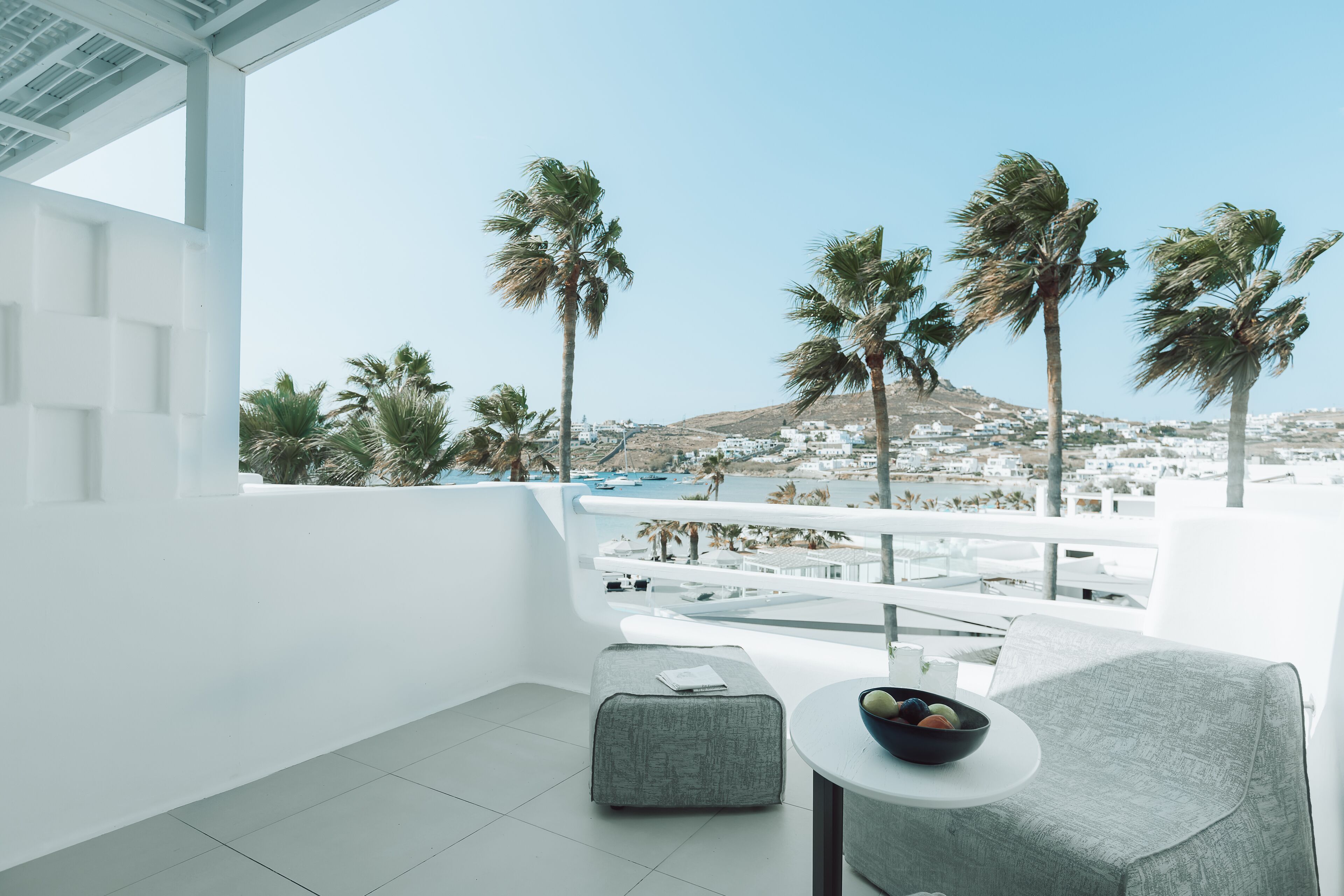 A balcony with a view of a coastal town, palm trees, and a mountain in the distance.