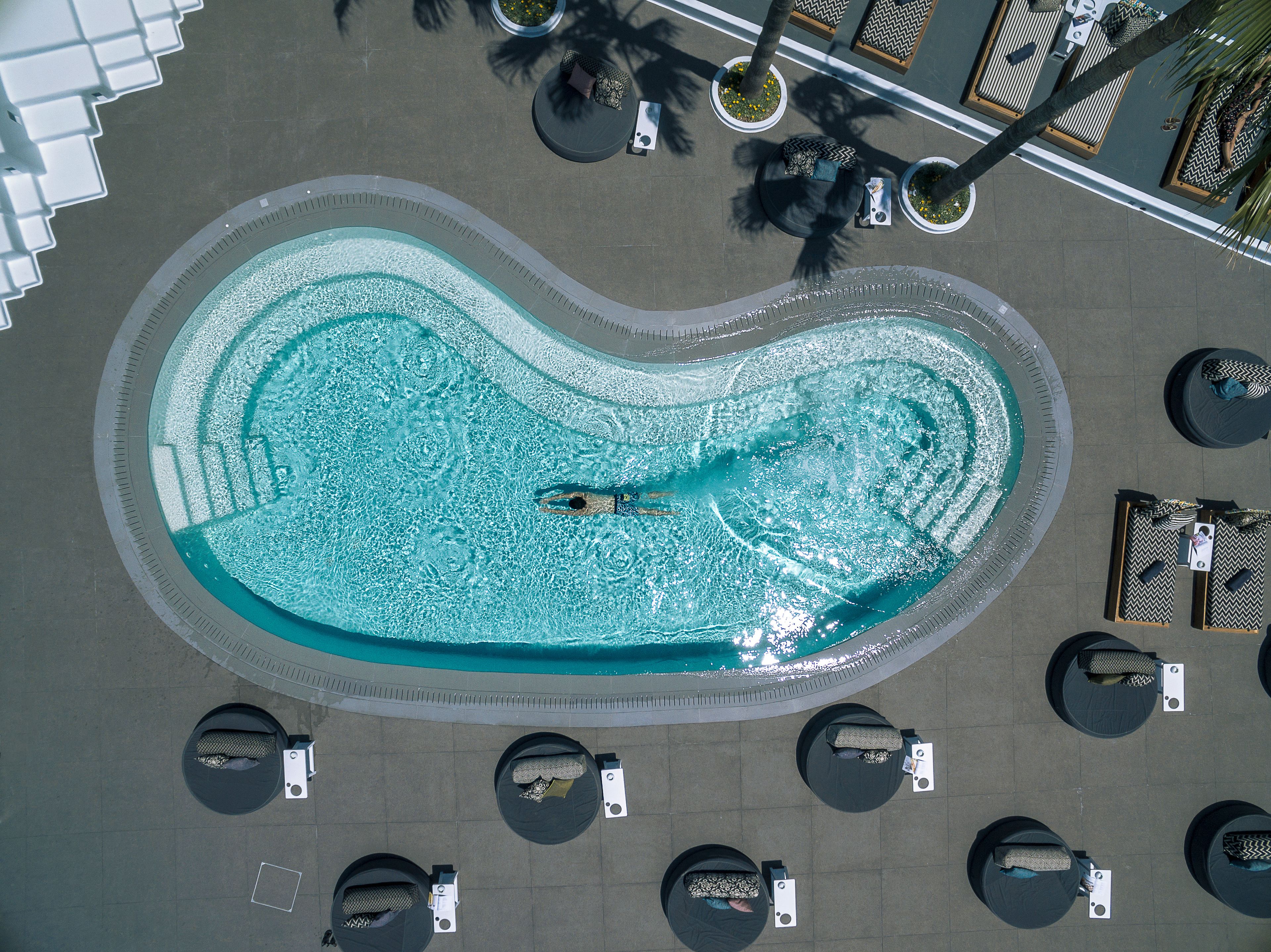 Vista aérea de una piscina con una persona nadando, rodeada de sillones y mesas.