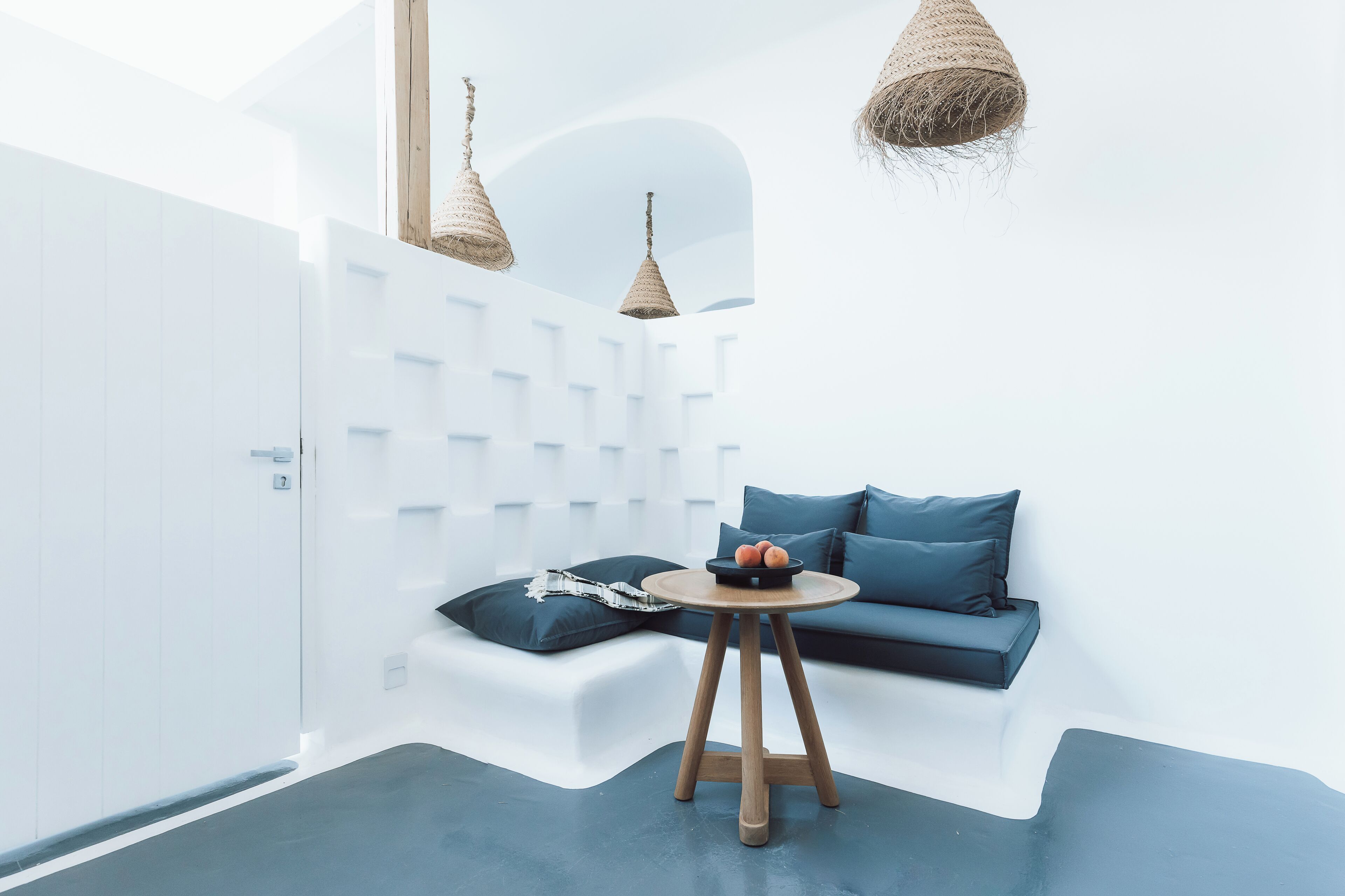 A modern room with a white wall, a blue sofa, a round wooden table, and hanging woven light fixtures.