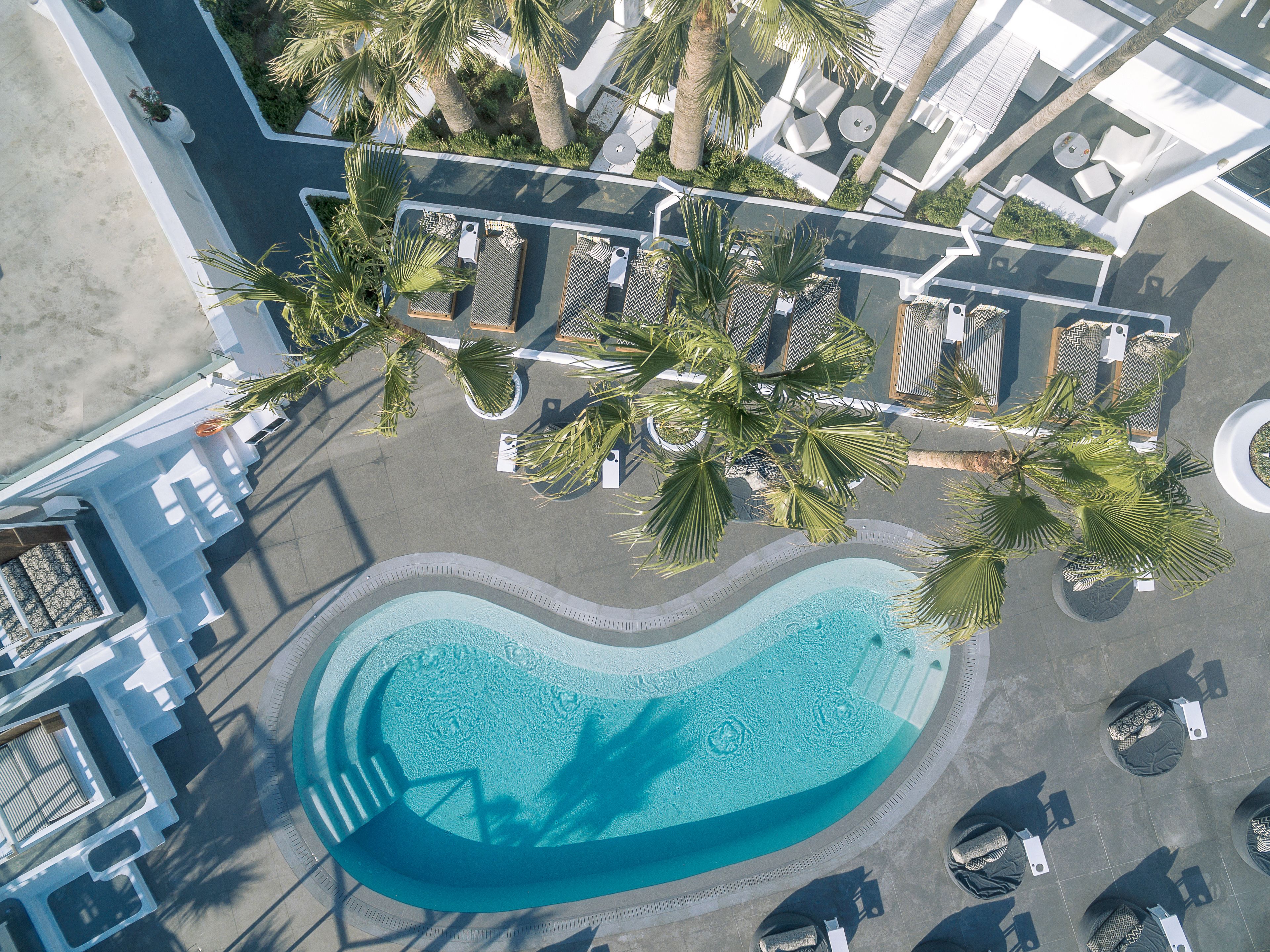 An aerial view of a resort with a swimming pool, lounge chairs, and palm trees.