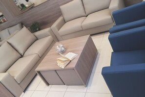 Una sala de estar moderna con un sofá seccional color beige, una mesa de centro de madera con libros y un objeto de vidrio, y sillones azules.