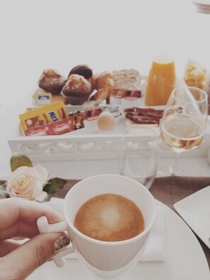 Una taza de café con un diseño artístico de latte, una bandeja de pasteles variados y una copa de vino blanco sobre una mesa.