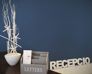 A desk with a white bowl containing branches, a grey box labeled "LETTERS," and a sign reading "RECEPCIO." - Hotel Carbonell (Llanca)
