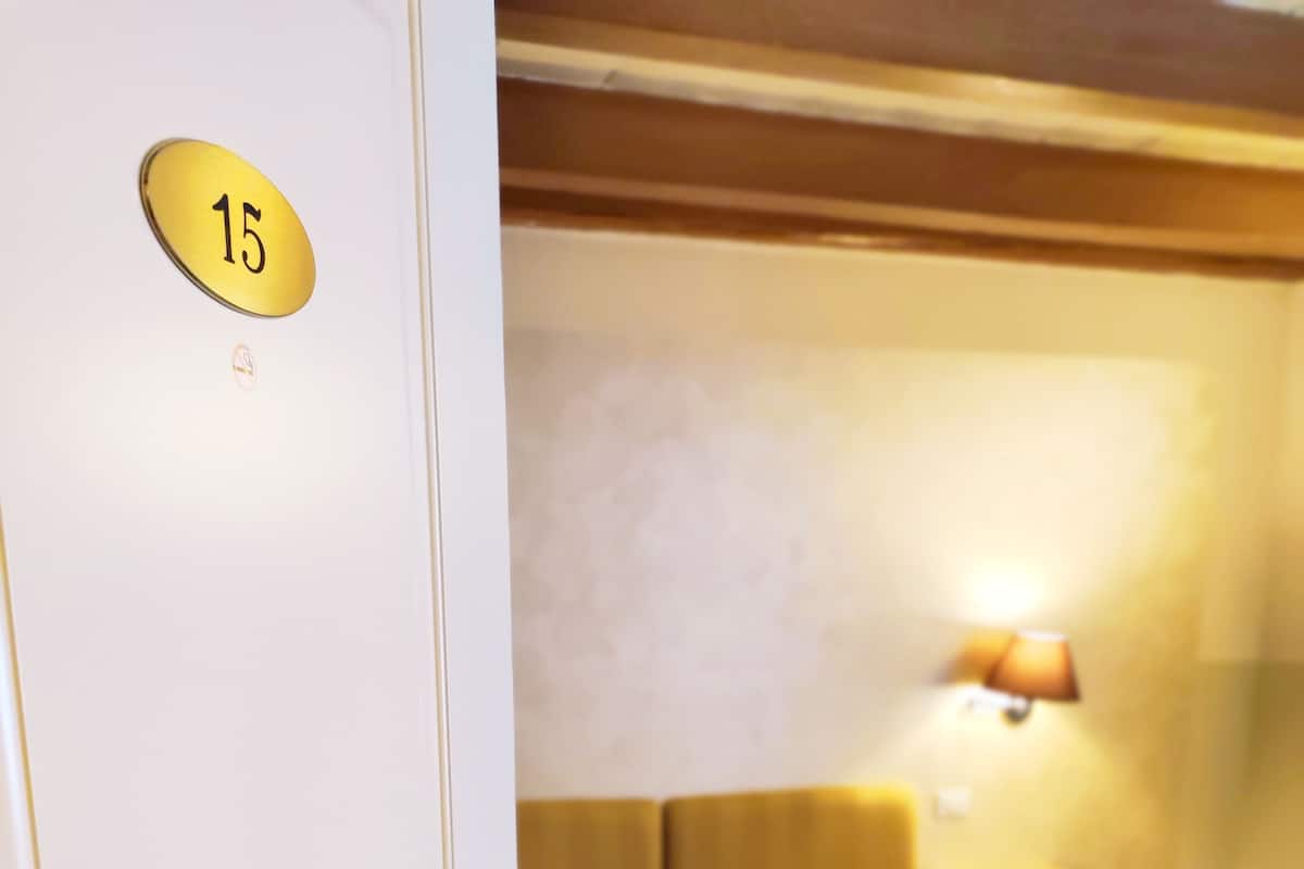 A hotel room with a bed, a nightstand, a lamp, and a door with a number plate.