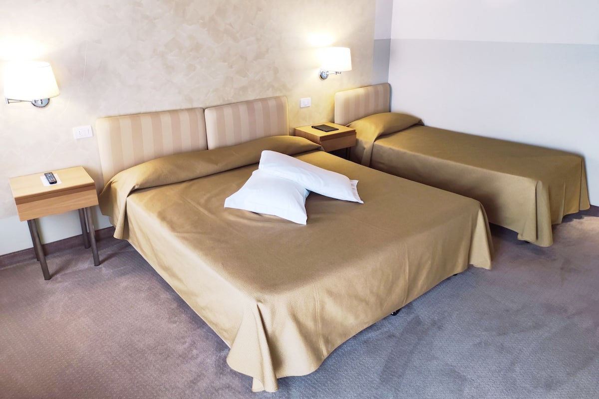 A hotel room with two beds, a nightstand with a lamp, and a wall-mounted light.