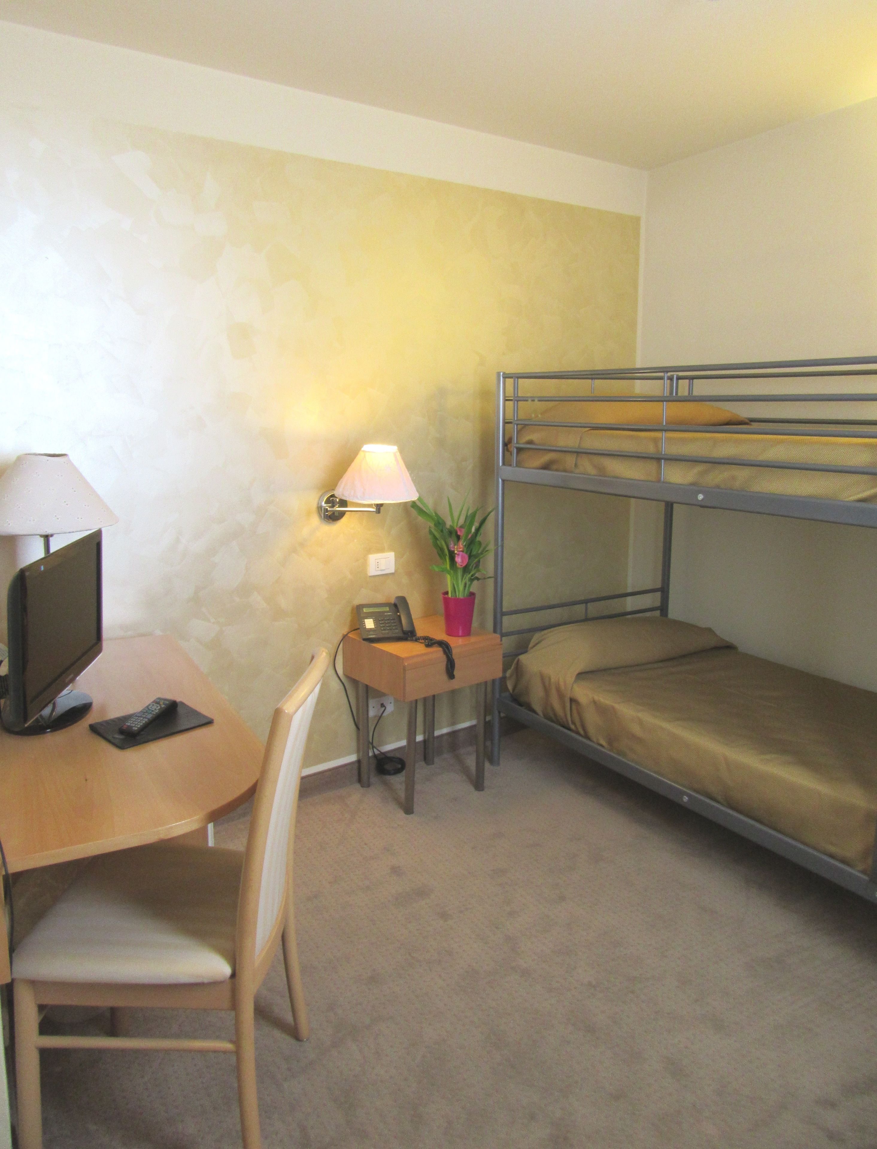 A small, compact room with a bunk bed, a desk with a computer and a lamp, and a chair.
