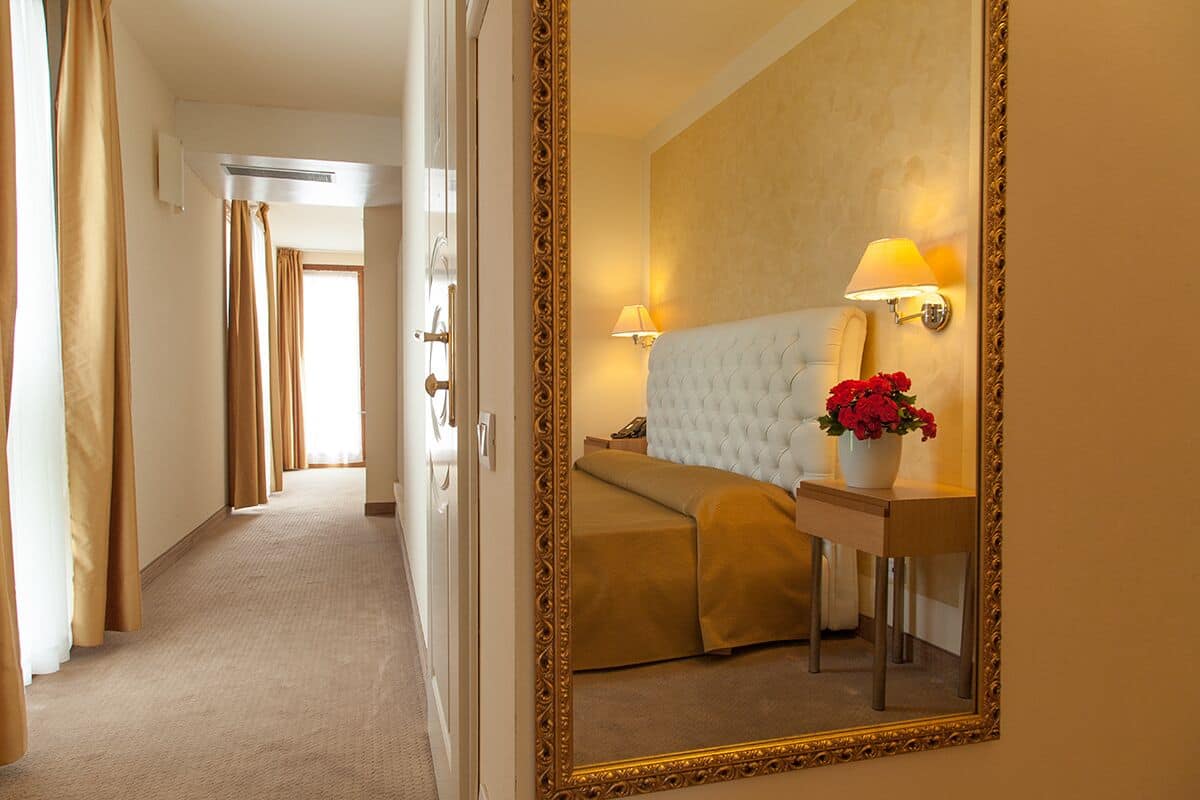 A hotel room with a bed, bedside table, lamp, and mirror.