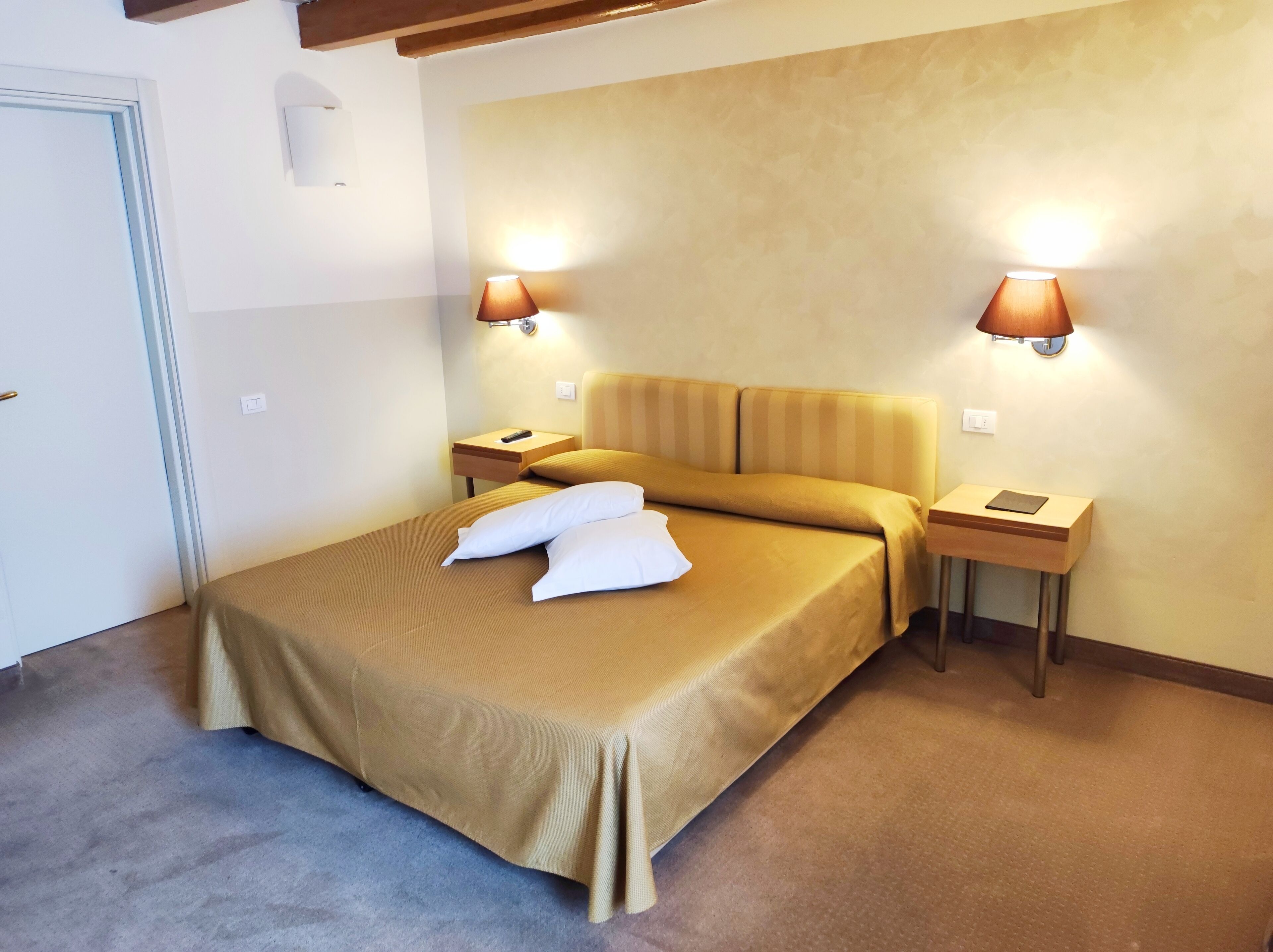 Une chambre d’hôtel comprenant un lit, deux tables de chevet et deux lampes fixées au mur.