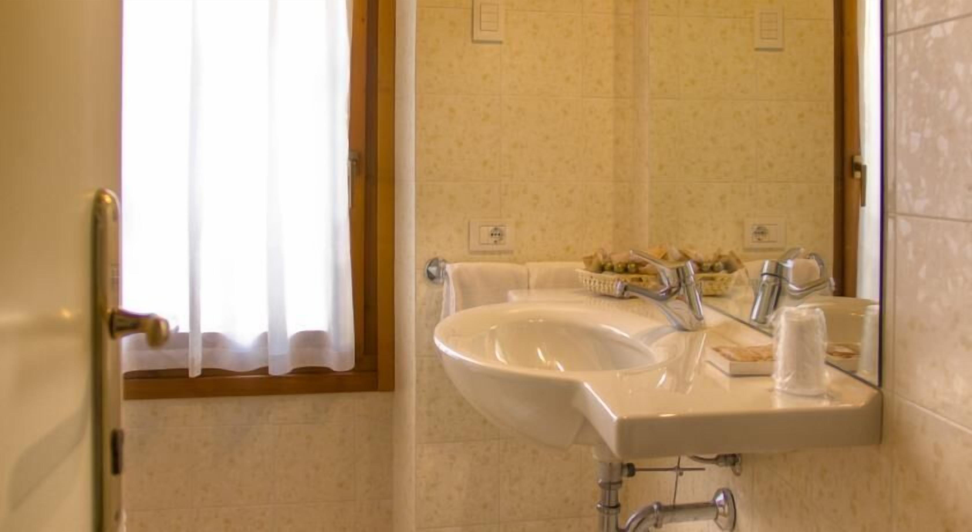 Casa de banho com lavatório, espelho e janela com cortinas.