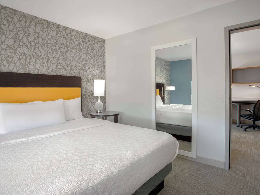 Habitació d'hotel amb un llit gran, un escriptori i una cadira. Hi ha un mirall a la paret i una taula petita amb una làmpada.