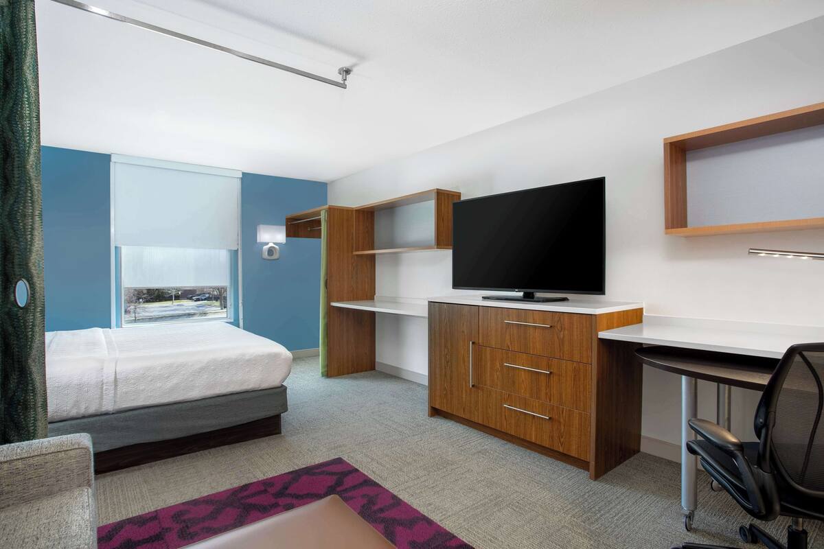 Habitación de hotel moderna con cama, escritorio, televisor y ventana con vistas al exterior.