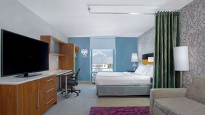 Una camera d'albergo con un letto, un divano, una TV, una scrivania e una finestra con tende.