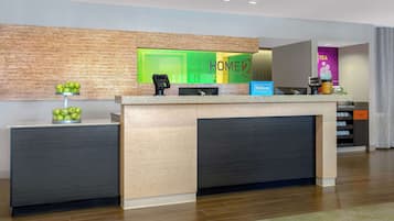 A hotel reception area with a modern design, featuring a reception desk, a coffee machine, and a sign for the hotel.
