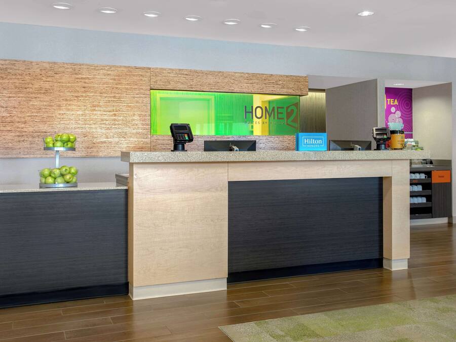 A hotel reception area with a modern design, featuring a reception desk, a coffee machine, and a sign for the hotel.