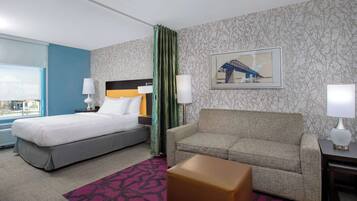 A hotel room with a bed, a sofa, a small table, and a window with a view.