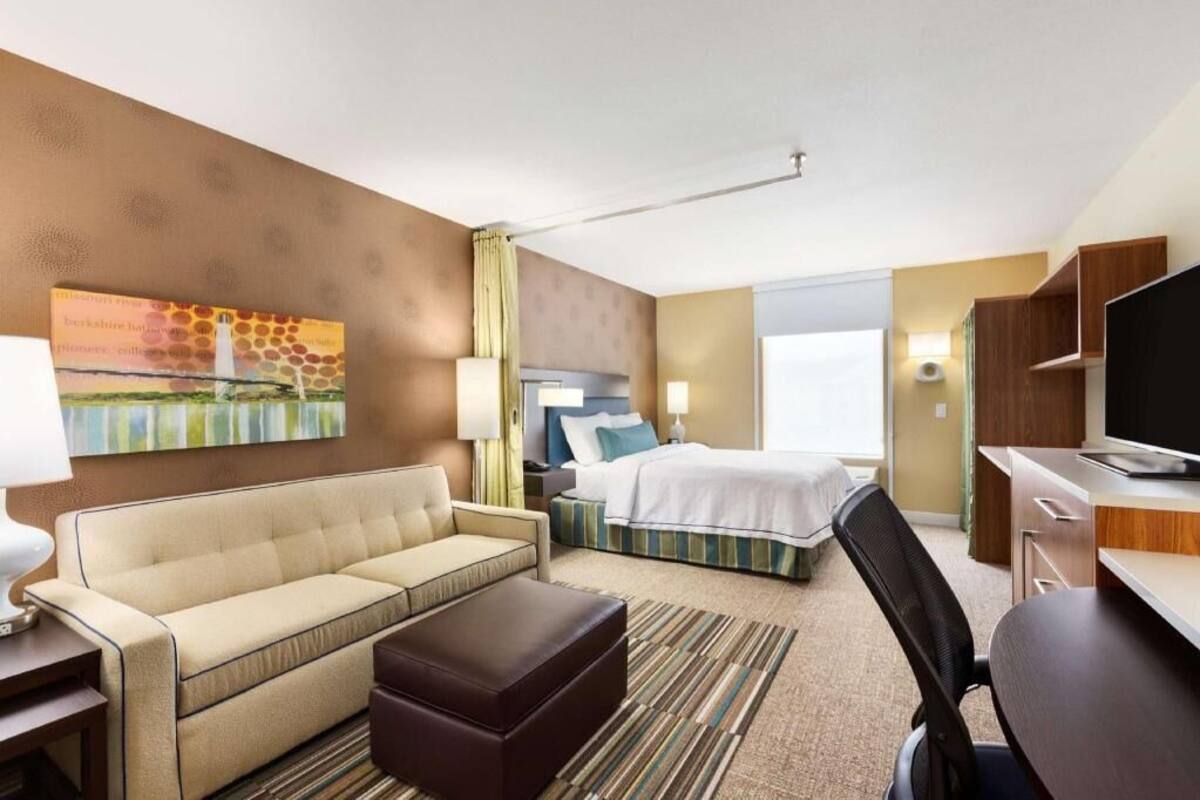 Habitación de hotel con sofá, cama, escritorio, televisor y obras de arte en la pared.