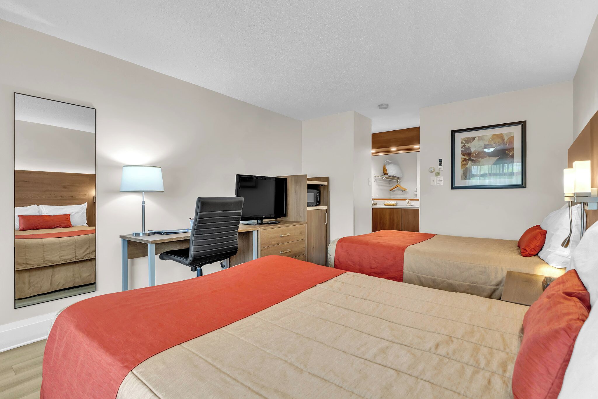 A hotel room with two beds, a desk with a computer, a television, and a mirror.