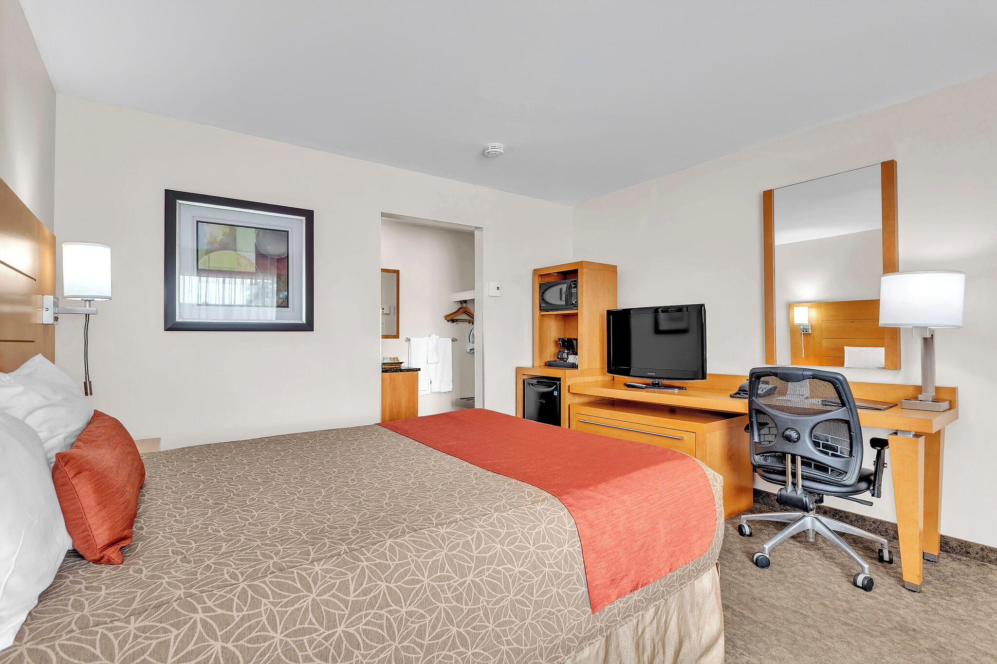 Ein Hotelzimmer mit Bett, Schreibtisch, Fernseher und Spiegel.