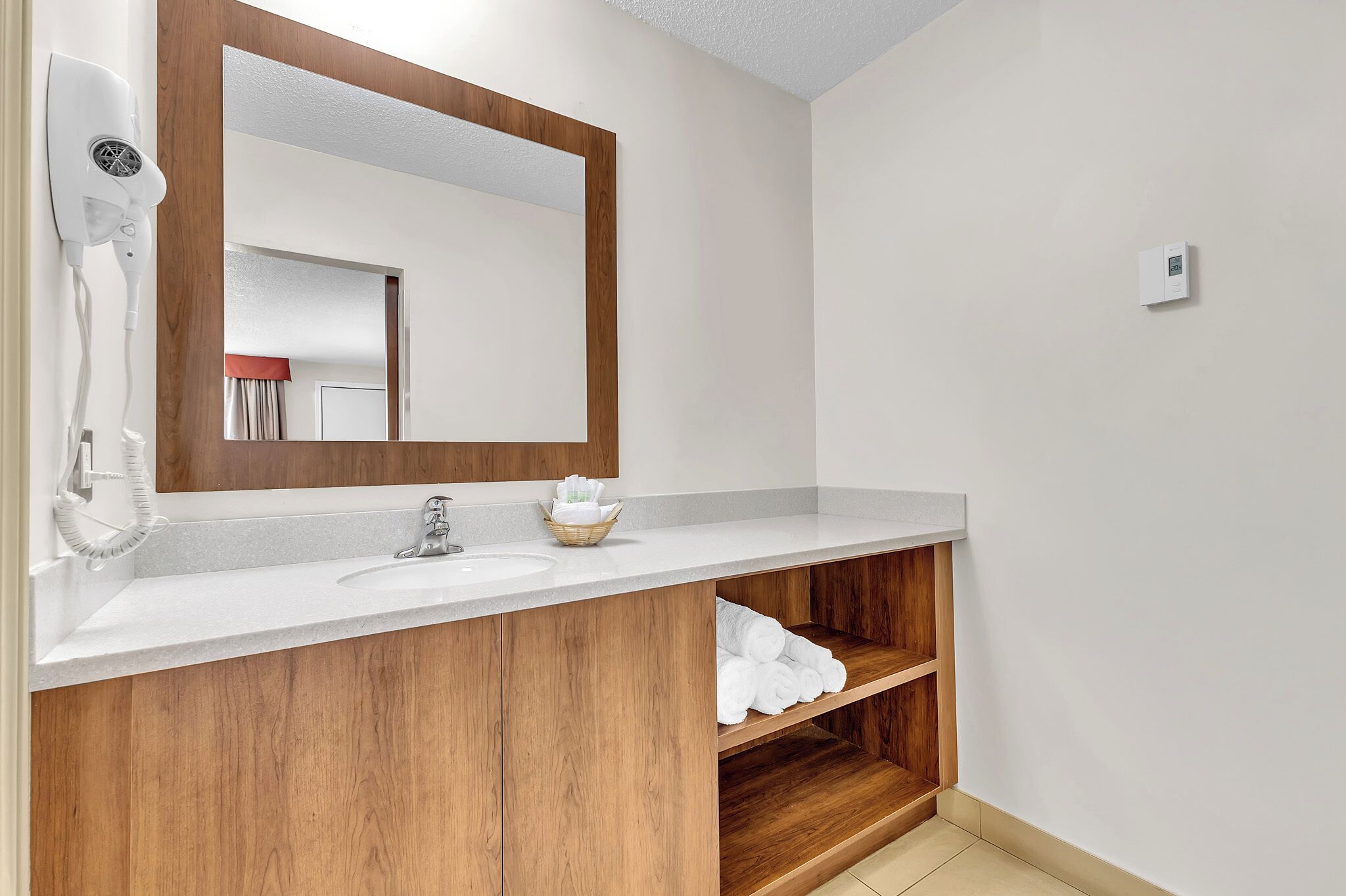 Un baño con tocador de madera, un lavamanos blanco, un espejo, un secador de pelo y un perchero para toallas.