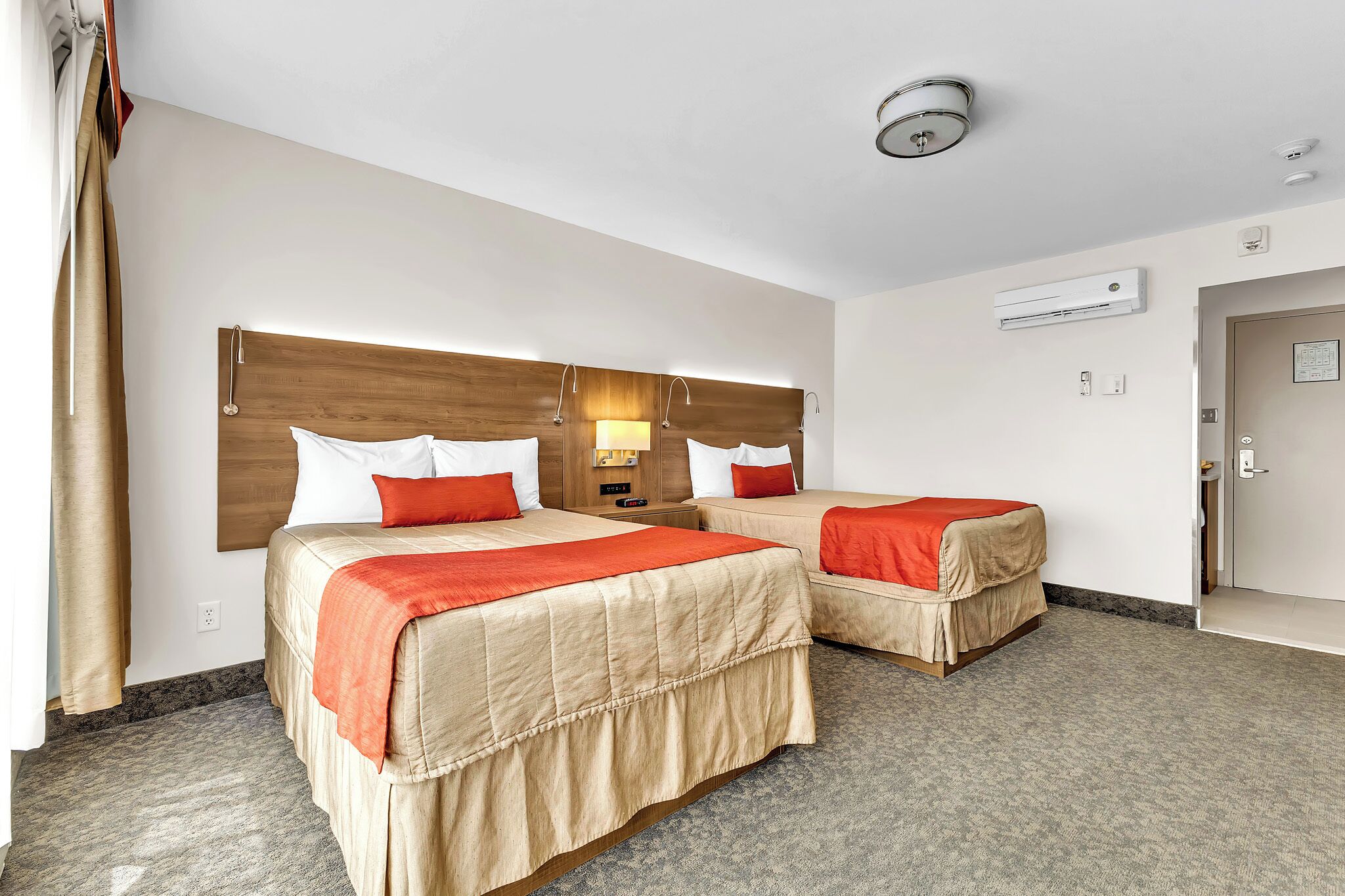 Een hotelkamer met twee bedden, een houten hoofdbord, een nachtkastje, een airconditioner en een deur.