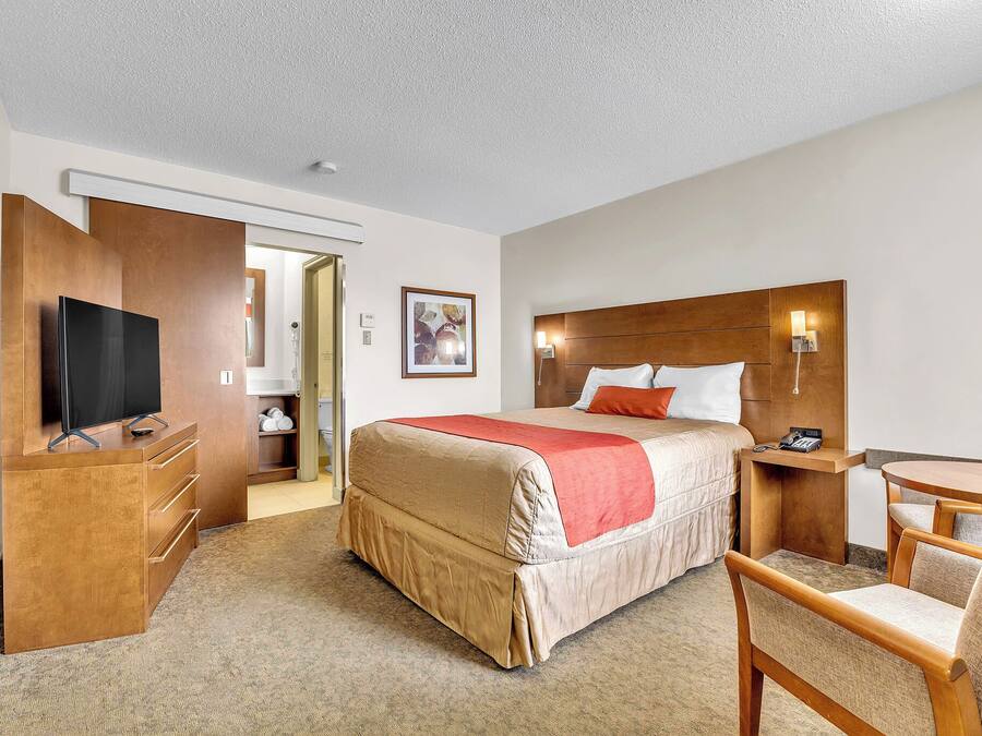Quarto de hotel com cama, secretária com televisão, cadeira e mesa pequena.