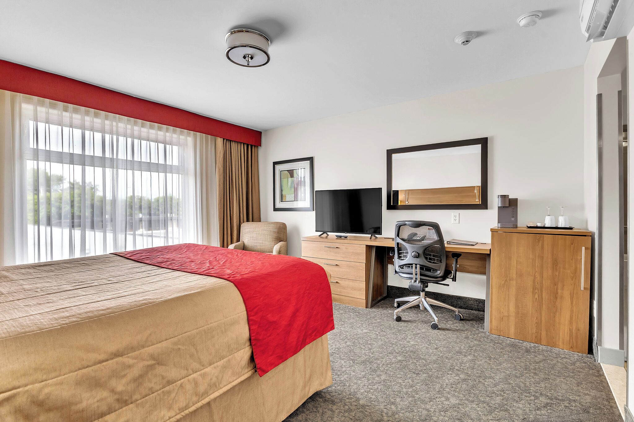 A hotel room with a bed, desk, chair, and a large window with curtains.