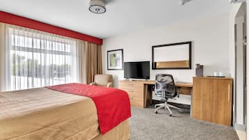 A hotel room with a bed, desk, chair, and a large window with curtains.