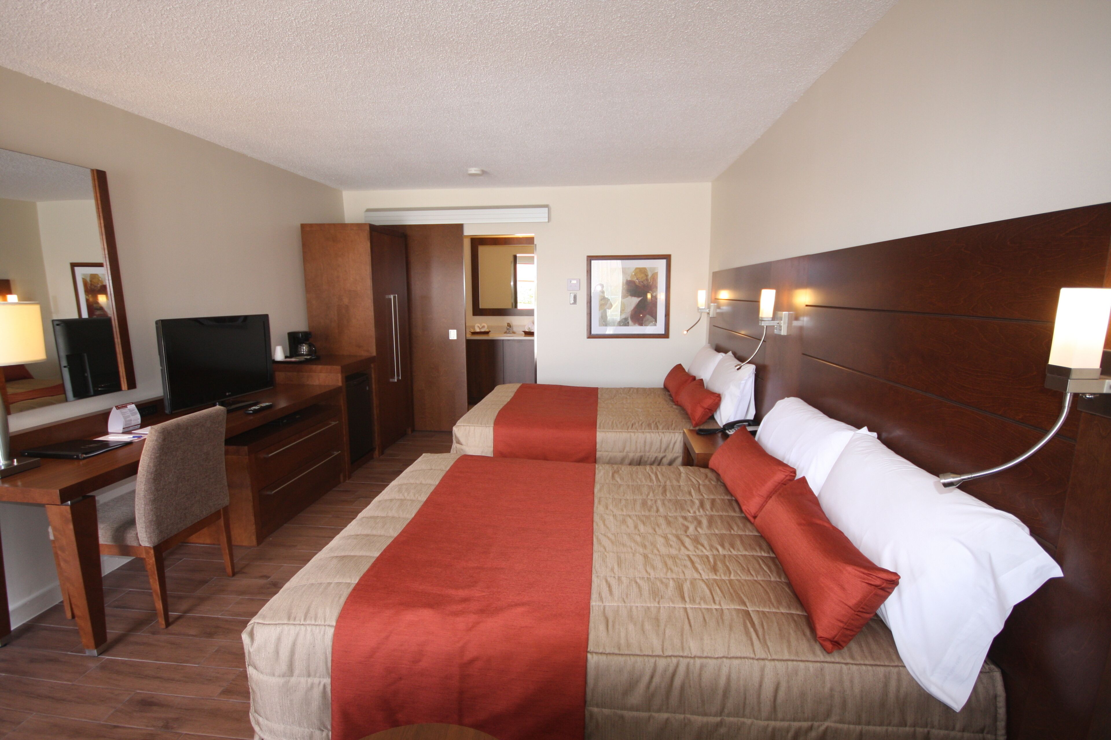 Una habitación de hotel con dos camas, un escritorio, un televisor y un espejo.