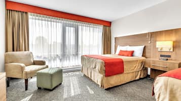 A hotel room with a bed, a chair, an ottoman, a nightstand, and a window with curtains.