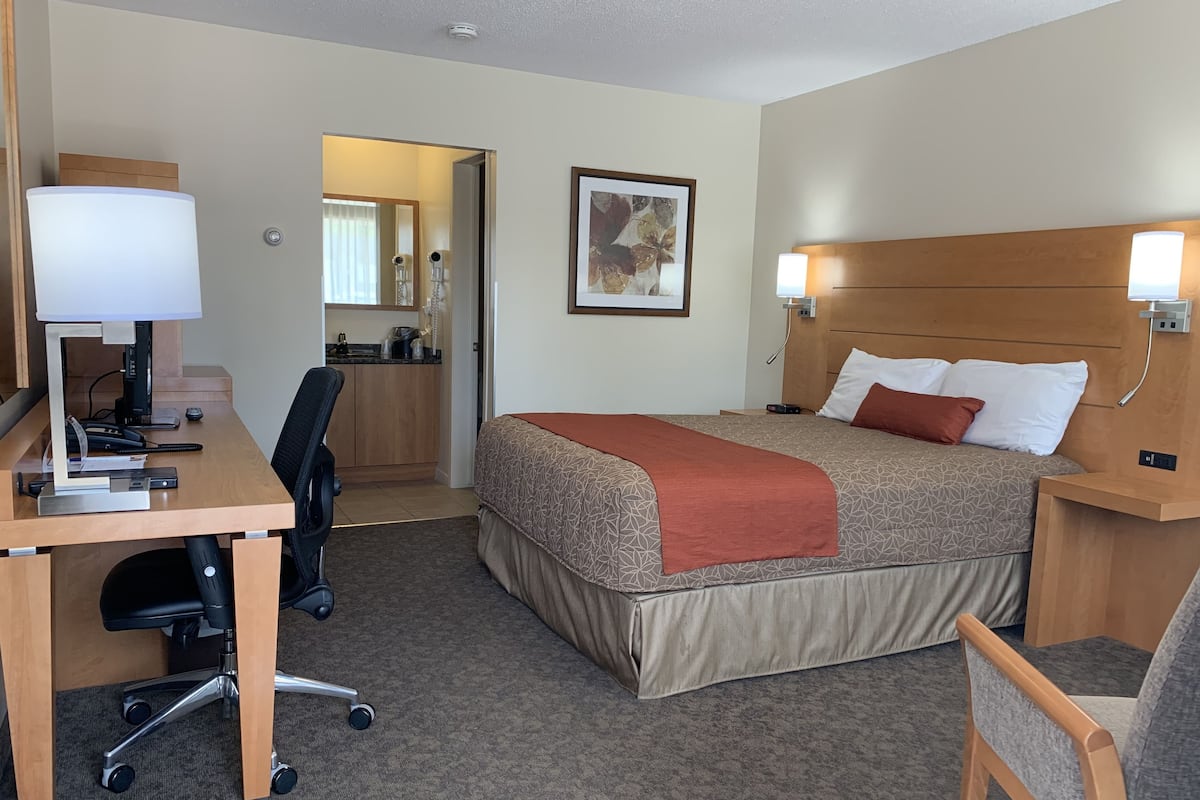 A hotel room with a bed, desk, chair, and a kitchenette.