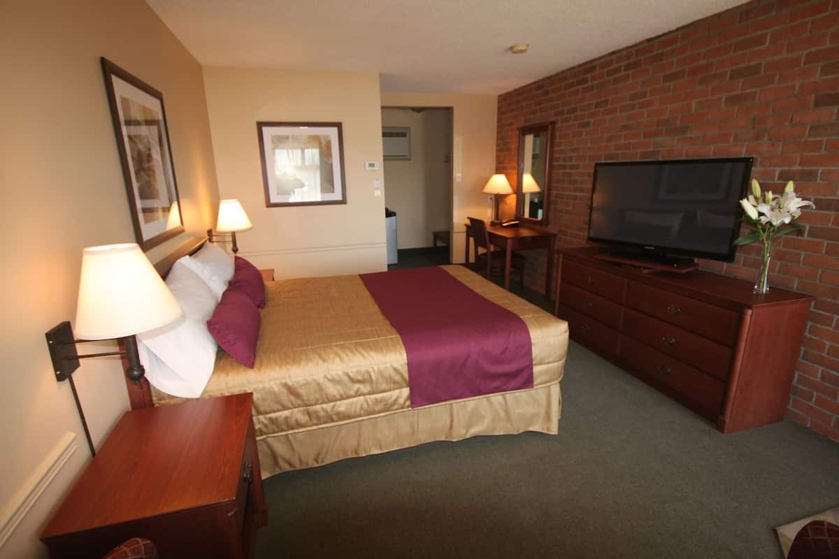 A hotel room with a bed, bedside lamps, a television, a dresser, and a brick wall.
