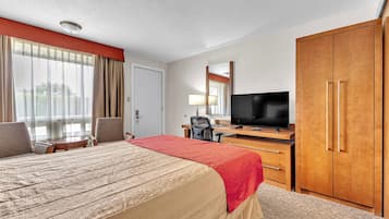 Een hotelkamer met een bed, een bureau met een televisie, een kledingkast en een raam met gordijnen.