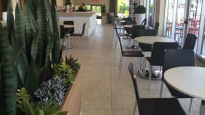Amplio espacio interior con varias mesas y sillas, un mostrador de recepción y grandes ventanales con vistas al exterior.