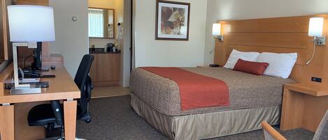 A hotel room with a bed, desk, chair, and a kitchenette.